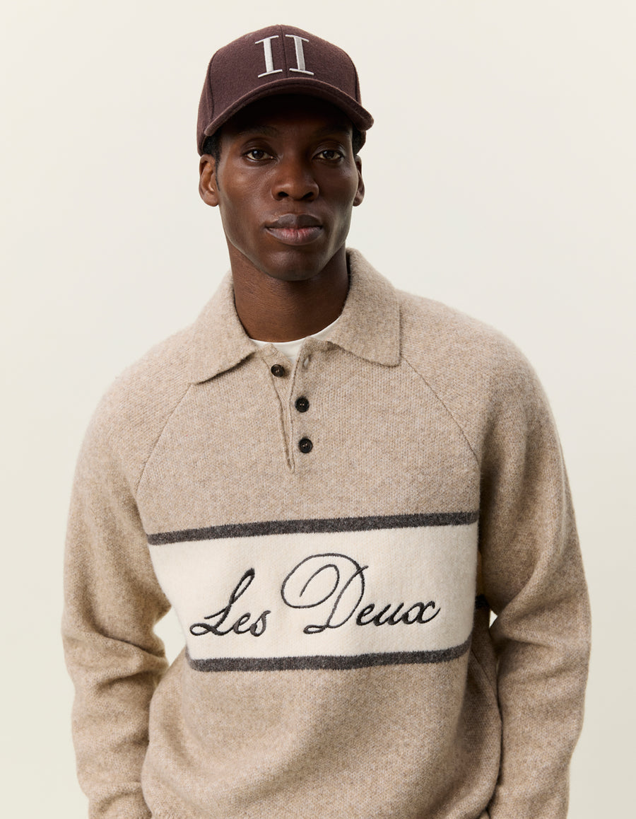 Nærbillede af model med kasket i Les Deux Signature melange strikpolo i Dark Sand melange med logostribe