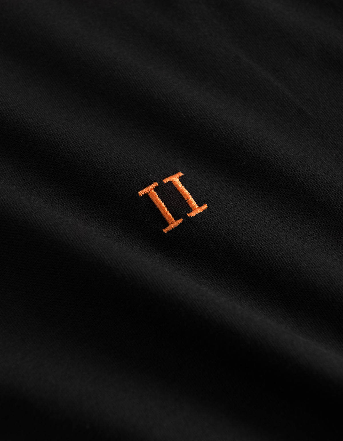 Detalje af orange broderet logo på Les Deux Nørregaard T-shirt i sort